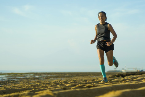 Eine Frau joggt mit Kompressionsstrümpfen am Strand entlang.