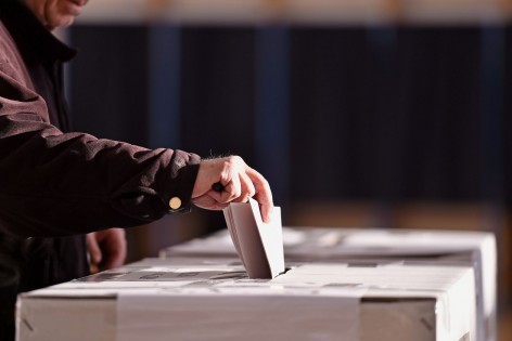 Eine Hand steckt einen Wahlzettel in eine Wahlurne