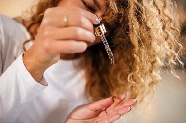 Frau mit rotbraunen Licken tröpfelt Haaröl in die Spitzen