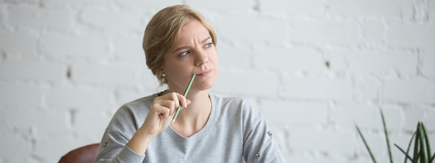 Junge Frau Anfang 20 überlegt, was sie vergessen hat. dabei hat sie einen Bleistift am Mundwinkel