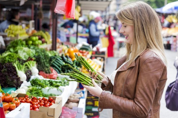 Eine Frau anfang 30 kauft auf dem Wochenmarkt grünen Spargel