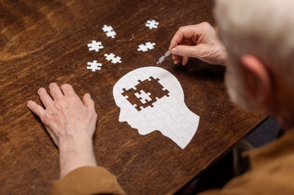 Ein Mann puzzelt auf einem Tisch. Das Puzzle an die Form eines Menschenkopfes.