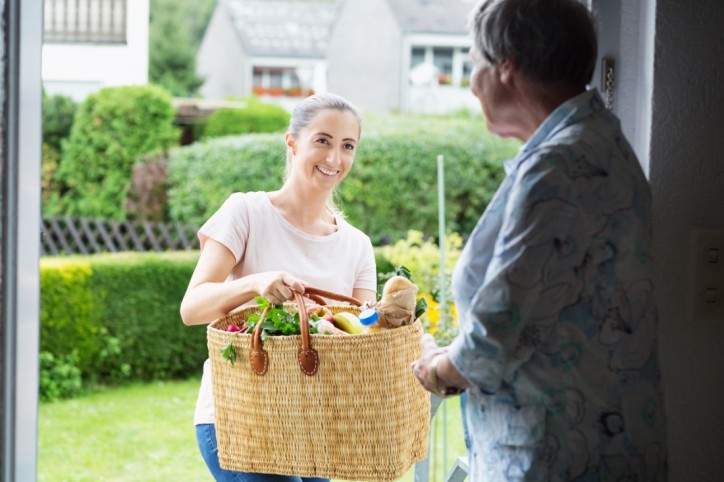 Eine Frau der Nachbarschafthilfe bringt einer Seniorin ihre Einkäufe