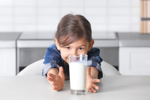 Ein etwa 5 jähriges Mädchen sitzt in der Küche und hat vor sich ein großes Glas Milch stehen.