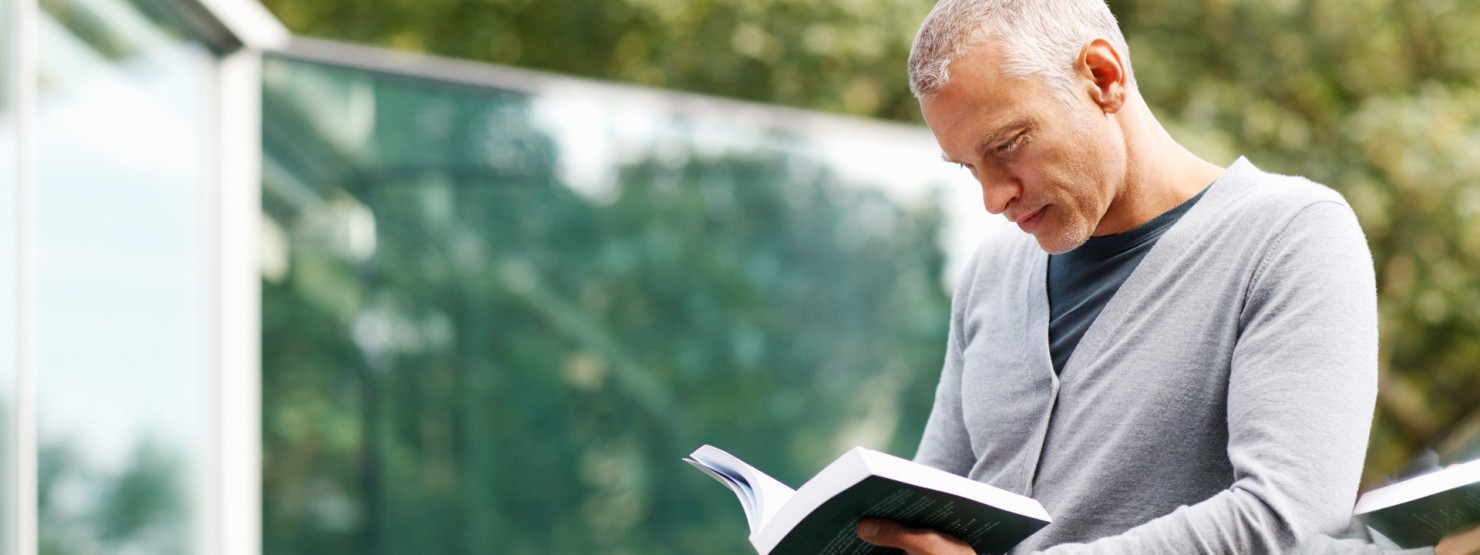 Ein Mann steht an einem Geländer und liest ein Buch.