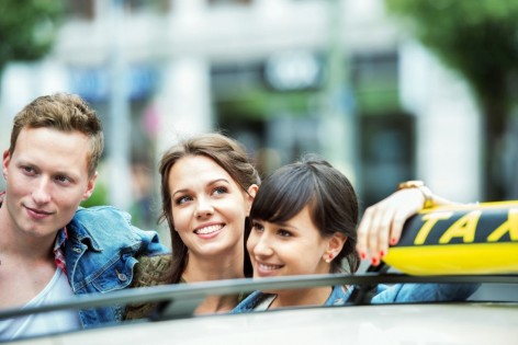 Drei Jugendliche lehnen an einem Taxi und lächeln.