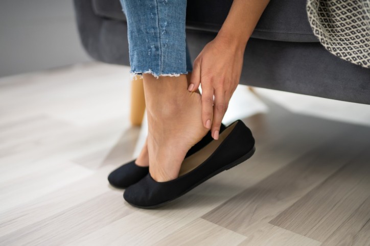 Eine Frau kontrolliert Ihren Fußballen nach dem Tragen von Ballerinas auf Hornhaut