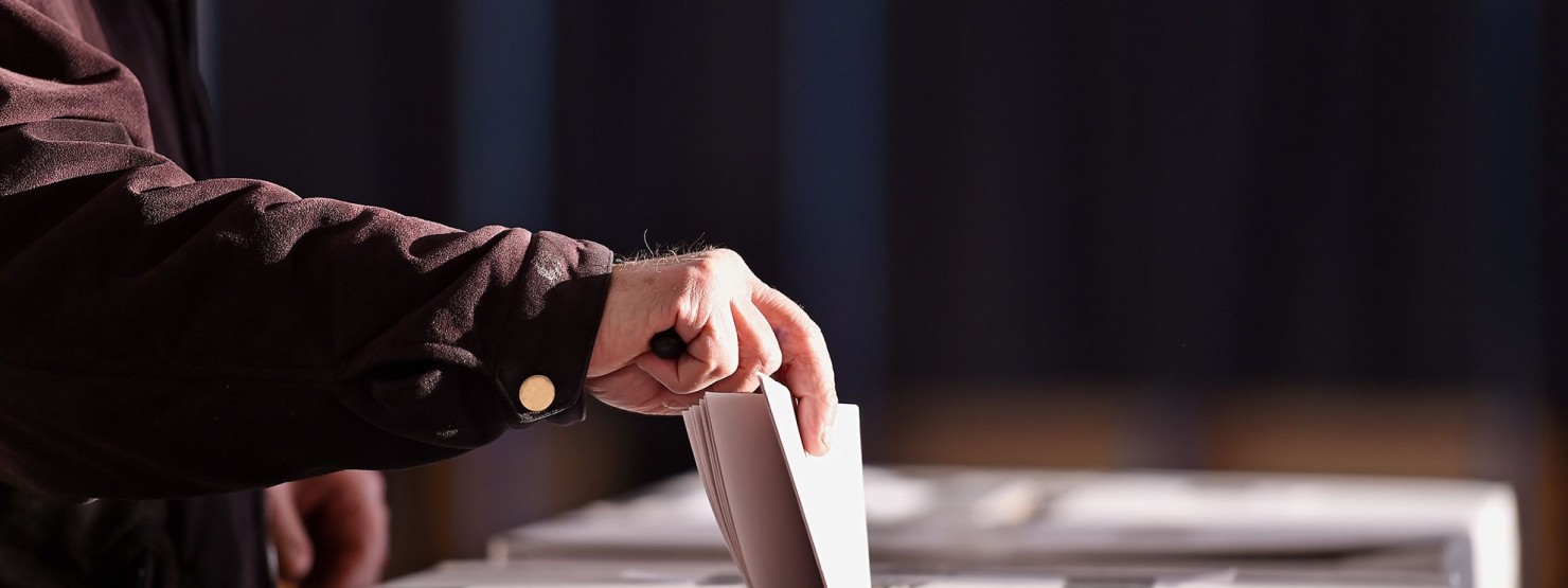 Eine Hand steckt einen Wahlzettel in eine Wahlurne