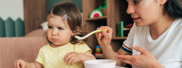 Ein wählerisches Kleinkind wird von seiner Mama gefüttert.