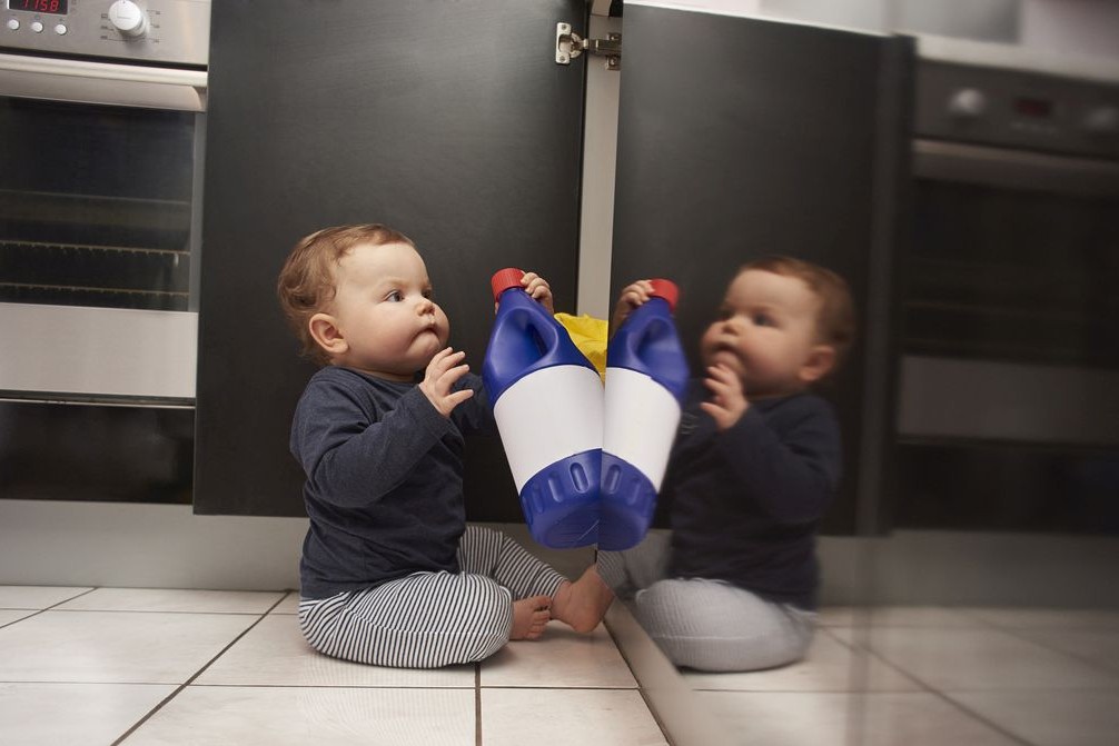 Ein Baby zieht eine Flasche Reiniger aus dem Küchenschrank.