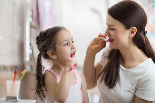 Eine etwa 6-jähriges Mädchen putzt mit Ihrer Mutter gemeinsam die Zähne.