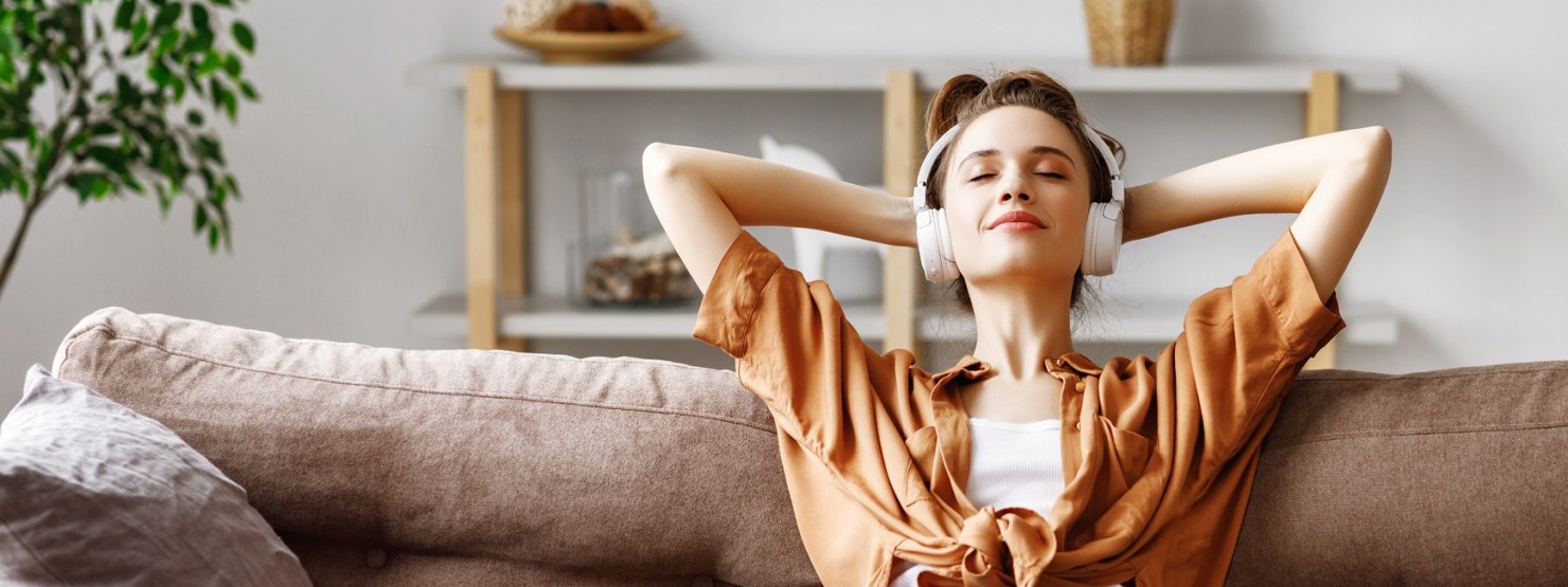 Frau sitzt entspannt mit Kopfhöhrern auf dem Sofa