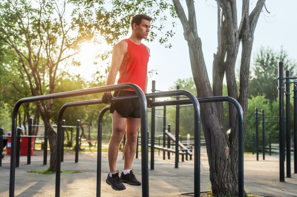 Ein sportlicher Mann führt während seines Morgen-Workout Dips an den Parallelstangen eines Calisthenics-Park aus.