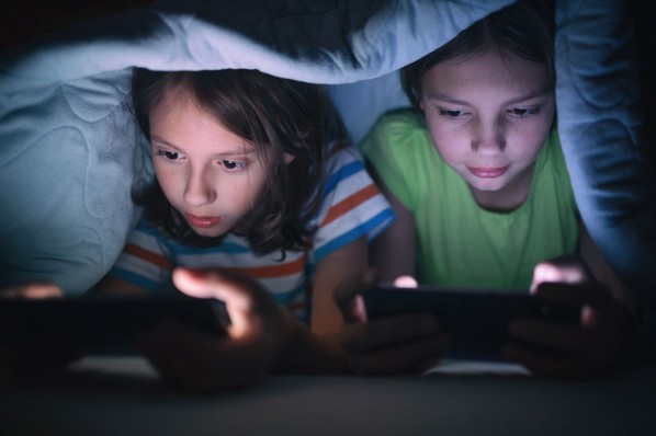 Zwei Kinder spielen unter der Bettdecke mit dem Handy