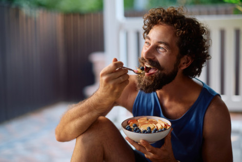 Ein sportlicher Mann isst nach seiner Ernährungsumstellung eine Schale mit Müsli und frischem Obst.