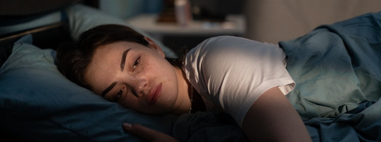 Eine etwa 25-jähriger Frau liegt nachts im Bett wach. Licht von draußen scheint in das Schlafzimmer und in ihr Gesicht.