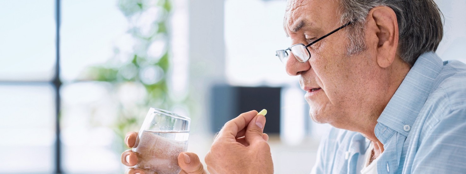 Ein circa 70-jähriger Mann führt eine Tablette zum Mund. In der anderen Hand hält er ein Wasserglas.