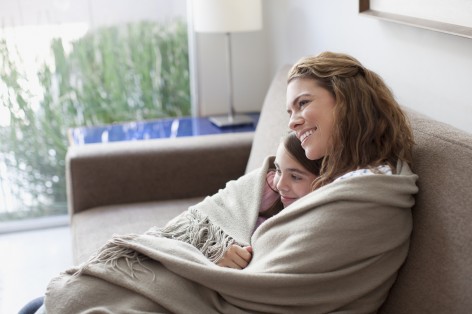 eine Mutter kuschelt mit iher Tochter auf dem Sofa. Sie sind in eine Decke eingewickelt