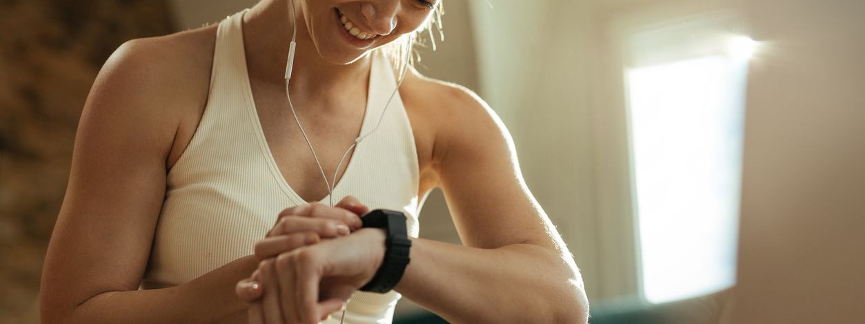 Junge Frau sitzt auf einer Sportmatte und schaut auf seine Fitnessuhr.