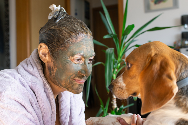 Eine Frau mit Heilerde im Gesicht und Haaren spielt mit ihrem Hund.