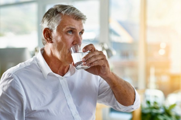 Ein etwa 60-jähriger Mann trinkt ein Glas Wasser.