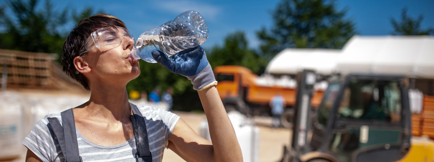 Eine Bauarbeiterin trinkt Wasser aus einer Flasche.