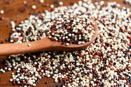 weißer, roter und schwarzer Quinoa liegen lose auf einem tisch mit einer Holzkelle
