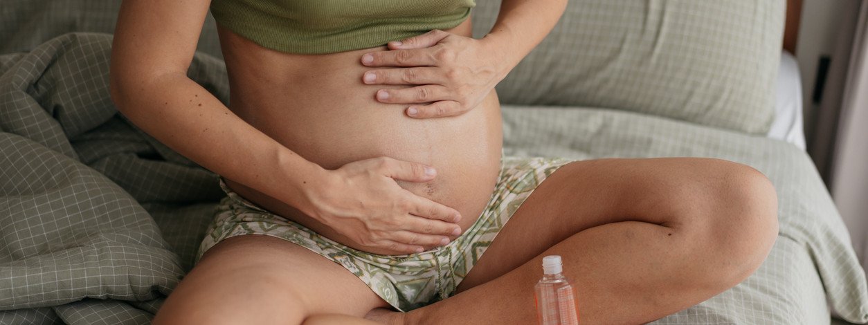 Schwangere Frau reibt mit Öl ihren bauch ein