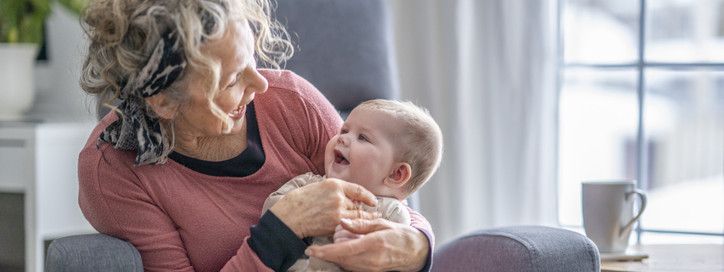 Eine Seniorin hält ein frisch gegen RS-Virus geimpftes Baby auf dem Schoß.