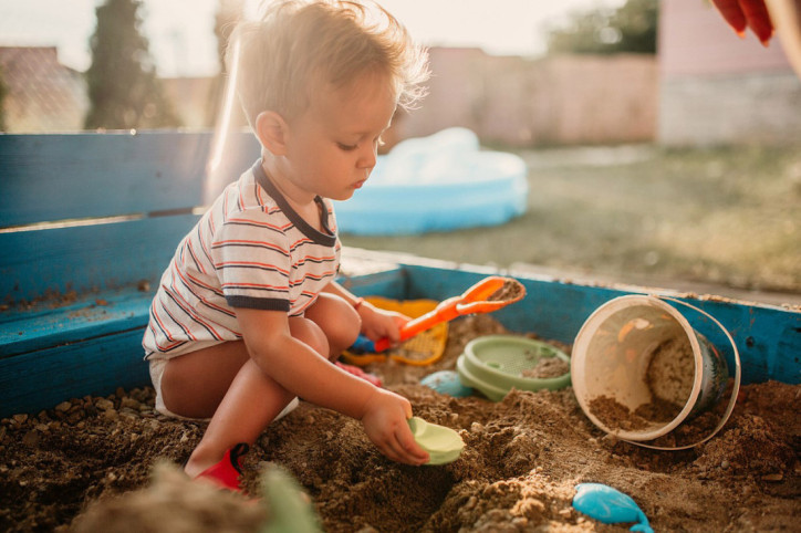 Ein kleiner Junge macht sich beim Spielen im Sandkasten die Hände schmutzig