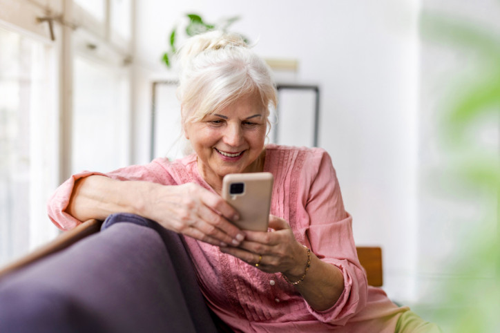 Eine Seniorin schaut freudig auf ihr Handy und ruft die Servicestelle 116 117 an.