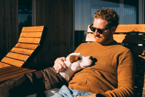 junger Mann mit Sonnenbrille und seinem Hund auf Sonnenliege