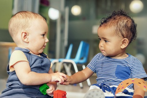 Zwei Kleinkinder schauen sich an und reichen sich die Hand.