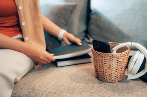 Junge Frau hält Notizbuch in den Händen. Neben ihr steht ein kleiner Korb mit Handy und Kopfhörern drin.
