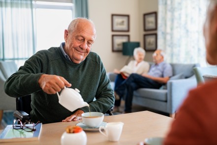 Ein Senior schüttet sich mit einer Kanne Tee in eine Tasse.