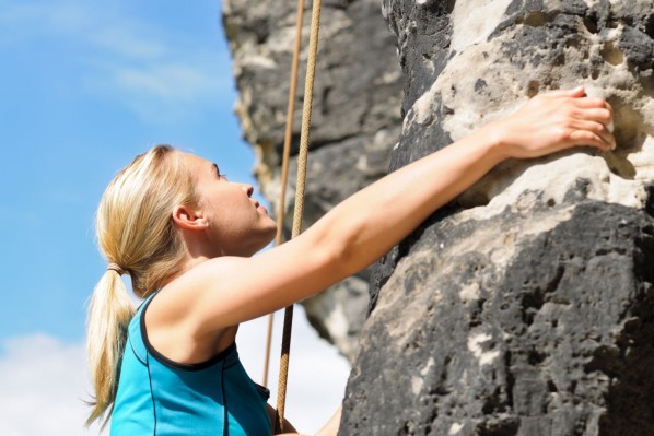 Eine etwa 30 jährige Frau klettert eine Felswand empor. Dabei schaut sie konzentriert nach oben.