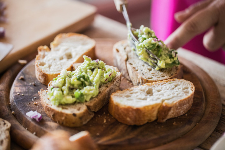 Hände streichen einen Avocadoaufstrich auf Brotscheiben.