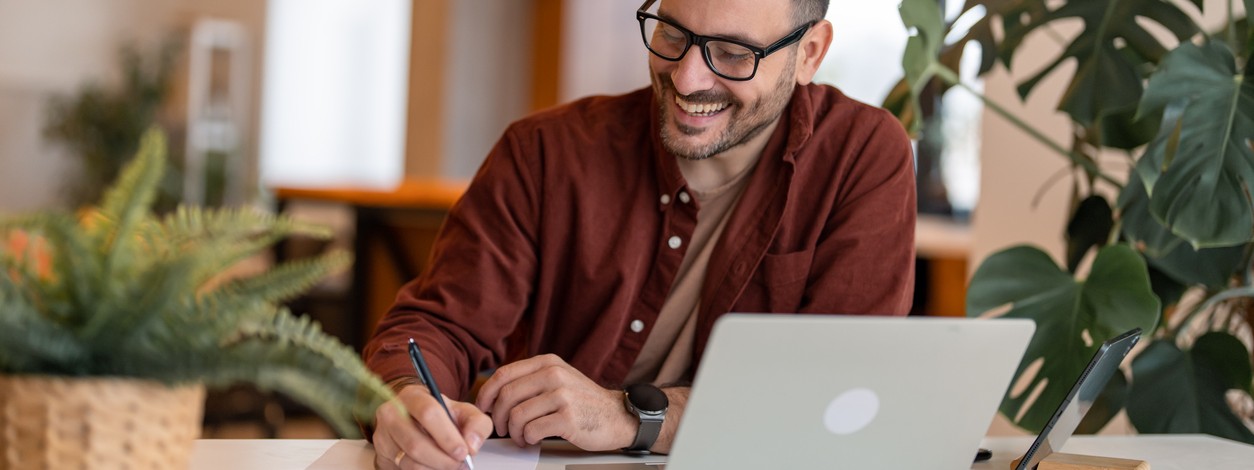 Ein Mann nimmt an einem Online-Seminar teil. Parallel schreibt er sich Notizen.
