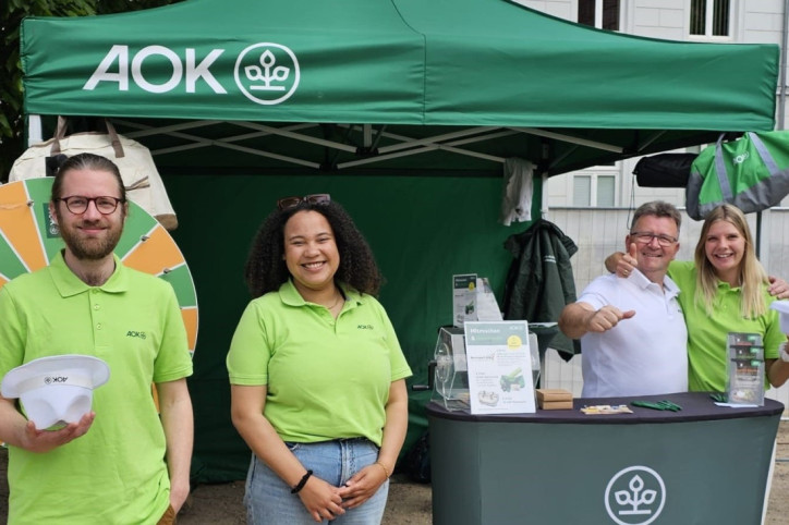 Mitarbeiter der AOK Sachsen-Anhalt stehen vor dem ihrem Stand auf dem Stadt- und Rosenfest in Bernburg