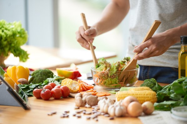 Eine etwa 25-jährige Person macht in einer Glasschüssel einen gemischten Salat mit Möhren und Mais.