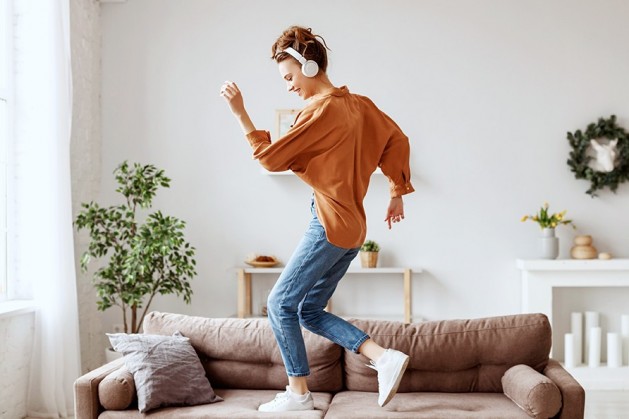 Frau mit Kopfhörern tanzt auf ihrem Sofa