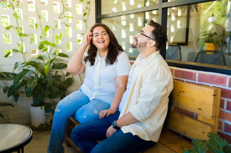 Ein Paar sitzt gemeinsam auf einer Bank und lacht ausgiebig.