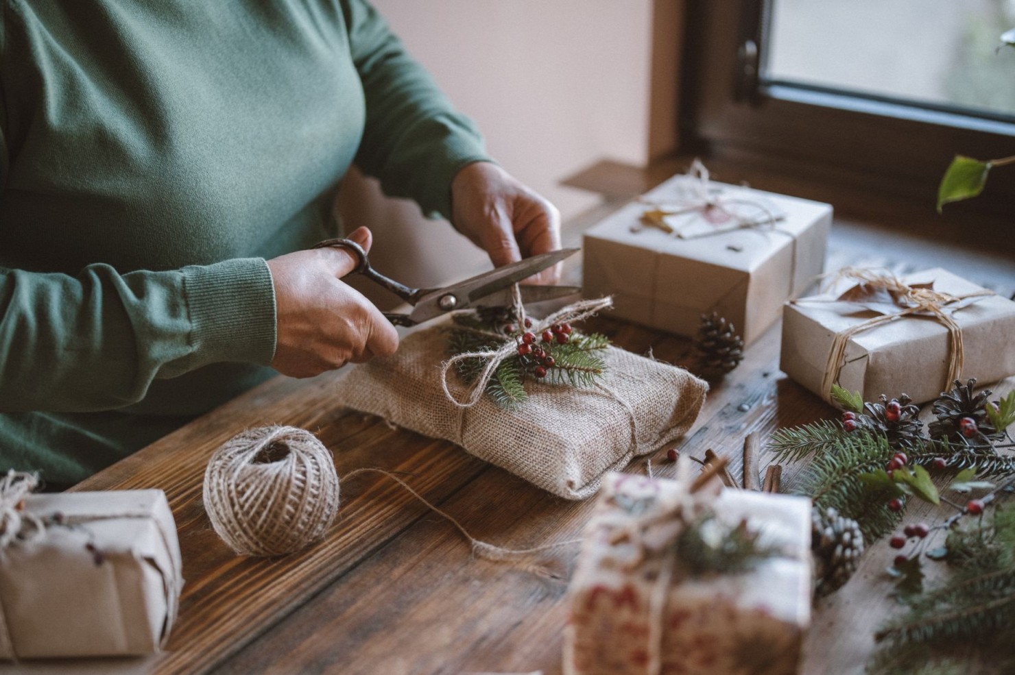 Eine Frau in grünem Pullover packt weihnachtsgeschenke ein. dafür nutzt sie nachhaltiges Verpackungsmaterial