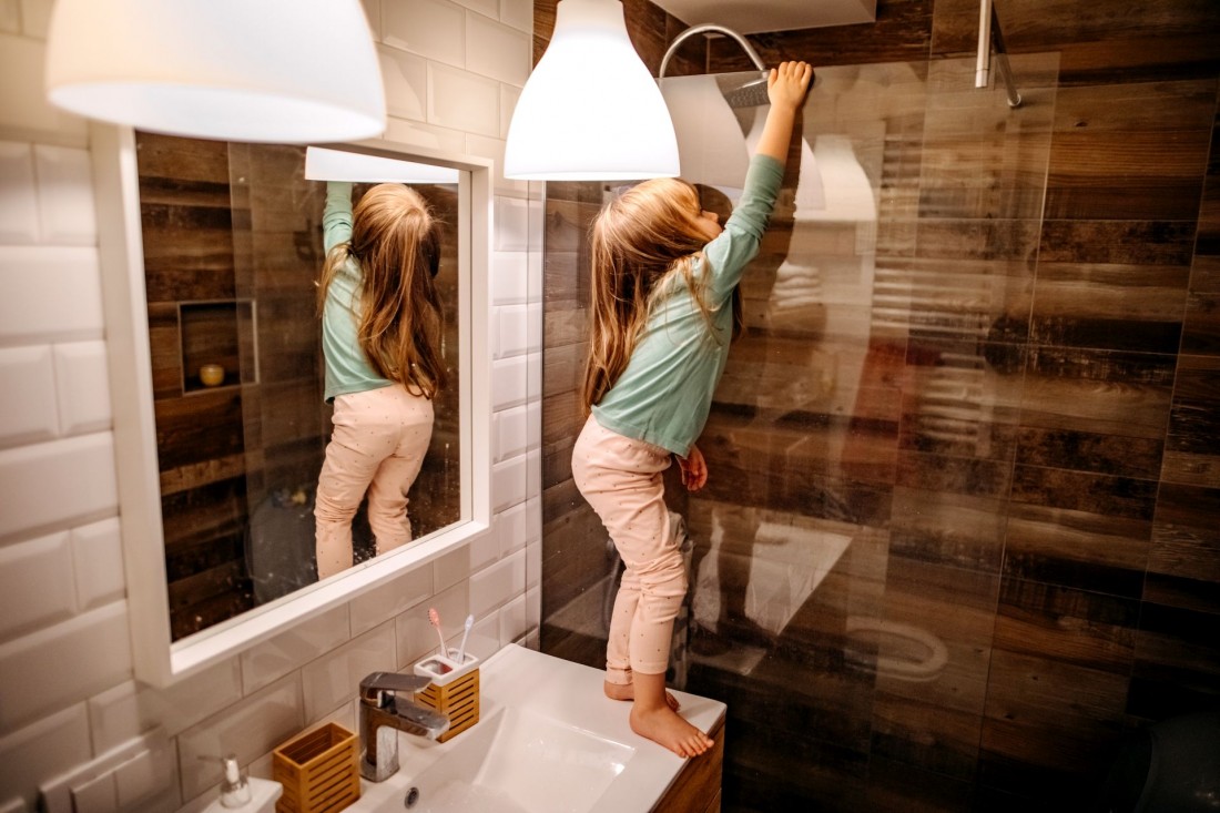 Ein etwa 3 jähriges Mädchen steht im Bad auf dem Waschtisch und klettert an der Duschwand hoch.