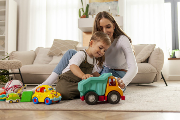 young mother plays with her little son with toys at home and smiles, 2-year-old boy plays with toy car with his parent, woman has fun with her child