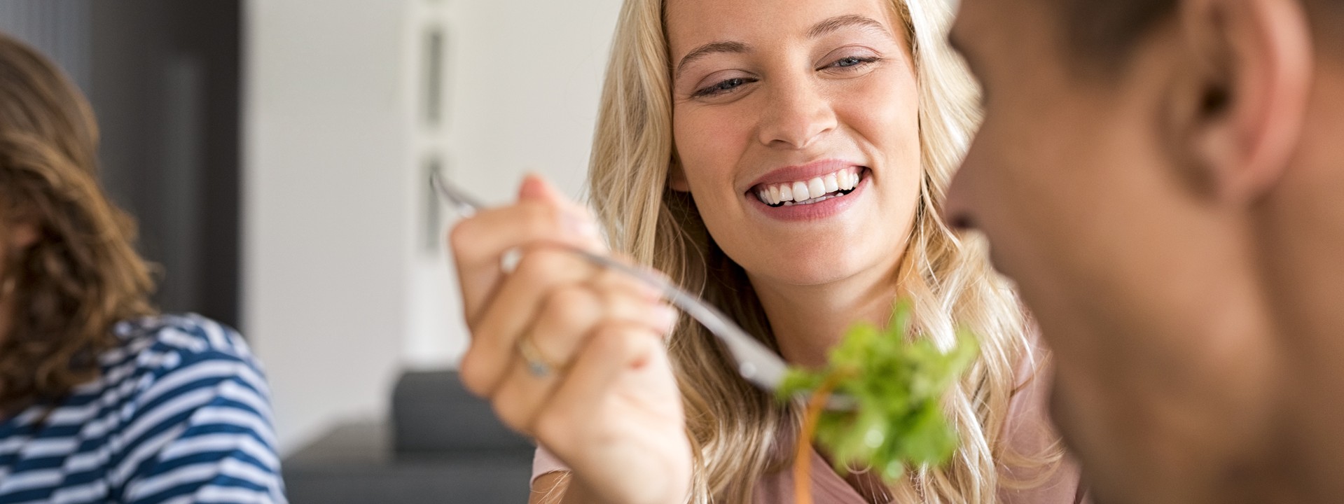 Eine circa 25-jährige Frau teilt eine Gabel ihres Salats mit einem Freund.