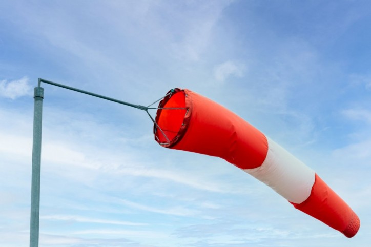 Ein Windsack hängt aufgeblasen an einem Mast. Es ist sehr windig. 