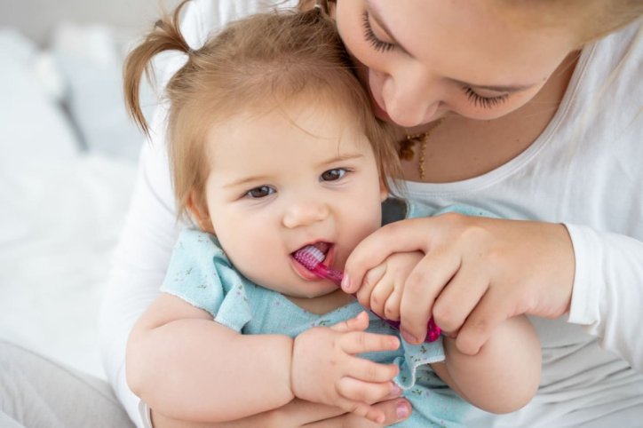 Eine Mutter putzt die ersten Zähnchen ihrer kleinen Tochter