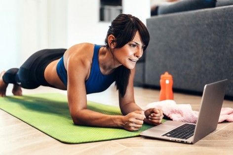 Strong sporty woman is doing working out at home and doing plank in front of her laptop