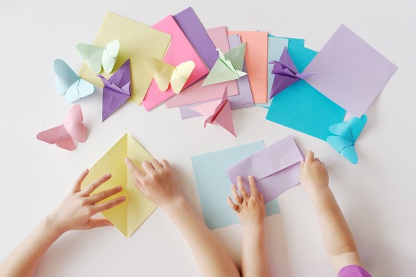 Kinder basteln aus bunten Papieren Origami-Schmetterlinge.